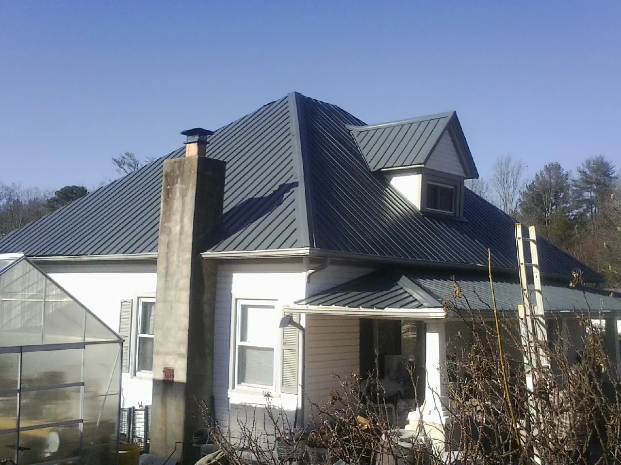 Dark blue standing seam metal roof on a white farmhouse with dormer — Slate & Tile Roof Repair by Roofing Brothers in Davy