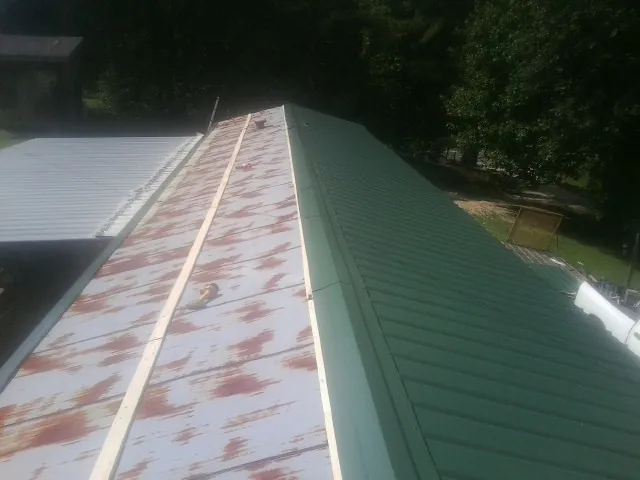 Old rusted panels beside newly installed green metal roofing — Wind Damage Roof Repair by Roofing Brothers in Davy