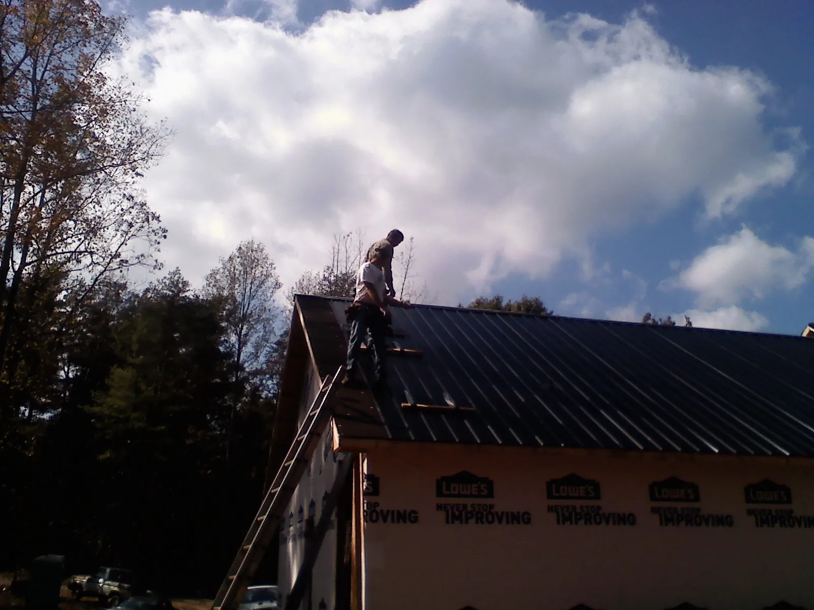 Roofer fastening dark metal panels high against a cloudy sky, from a Roof Inspection job in Davy